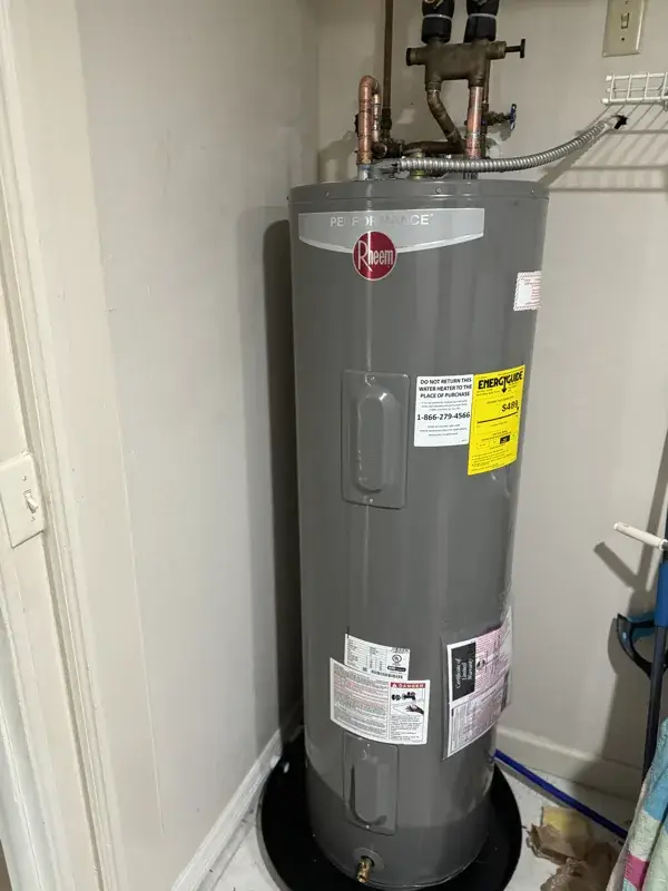 New tank water heater with copper connections sitting on a drain pan in a corner